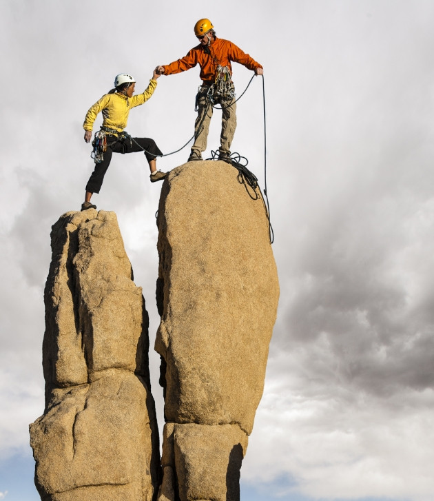 two people helping each other climb a mountain
